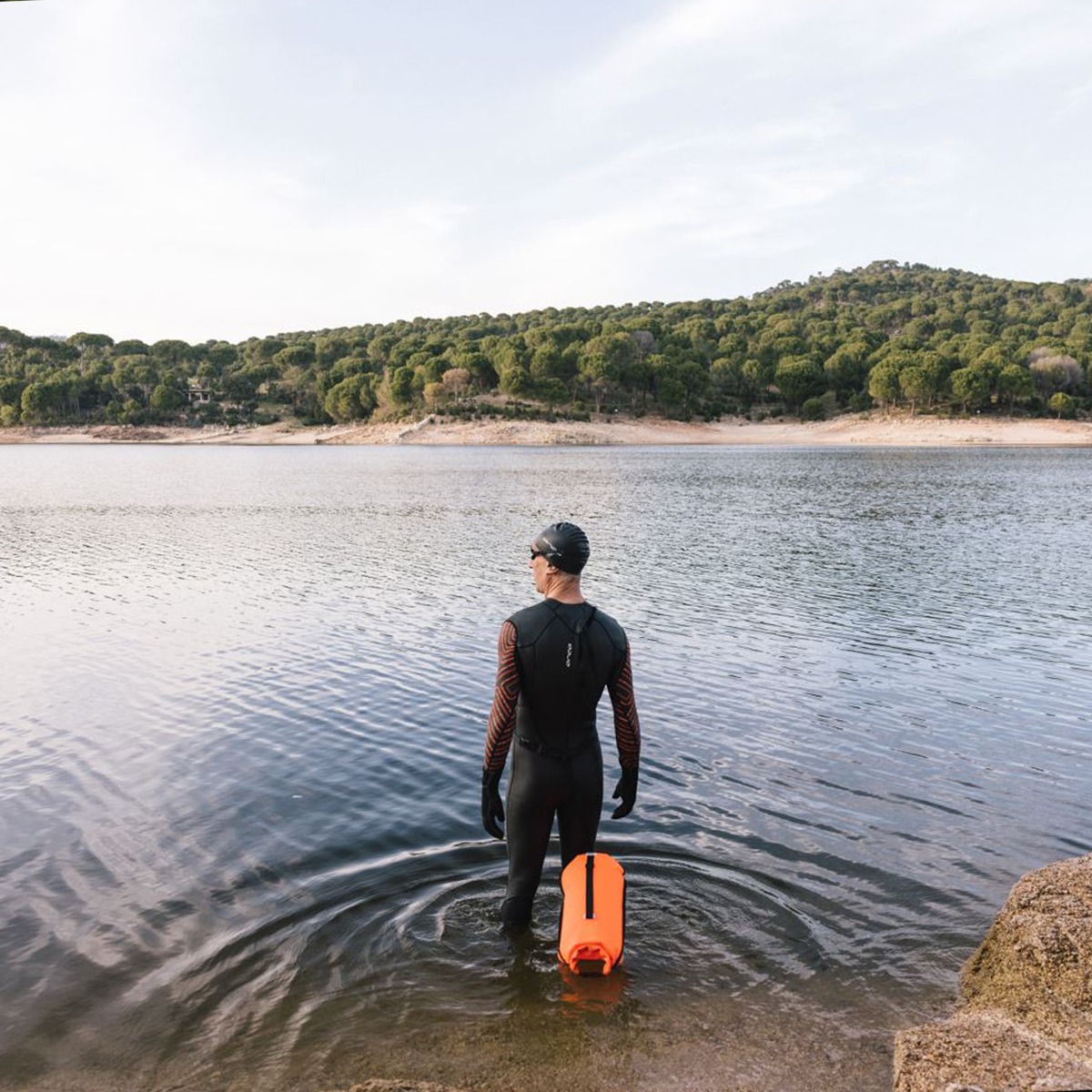 A man wearing a wetsuit stood in shallow water looking at a lake
