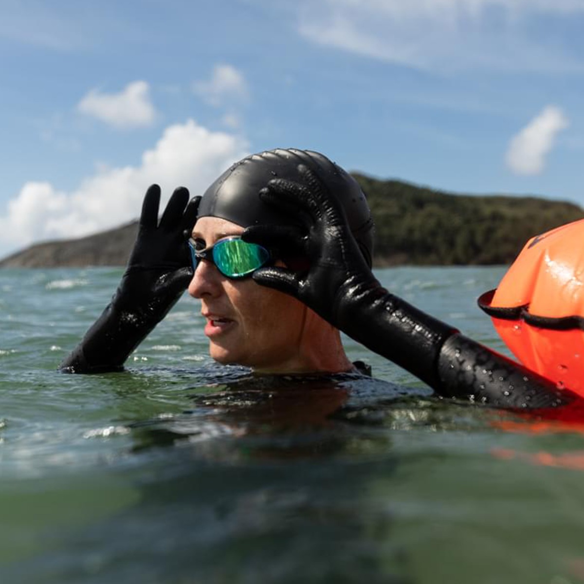 a woman swimming in the ocean, adjusting her goggles